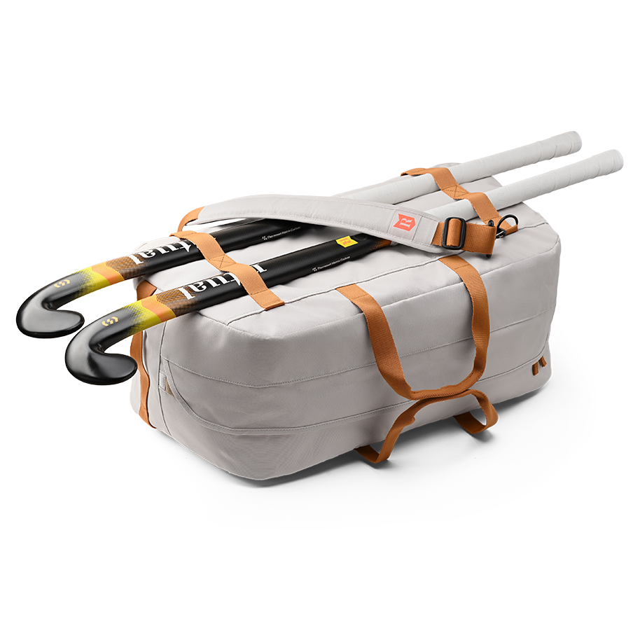 Ritual Calibre hockey duffle bag white with orange straps holding two hockey sticks, side view